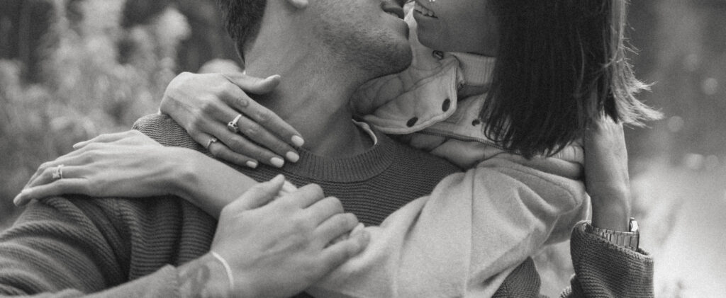 Close-up black-and-white image of Katya and Michael embracing during their French Alps elopement, highlighting their love and connection with tender details like their intertwined hands and engagement ring."