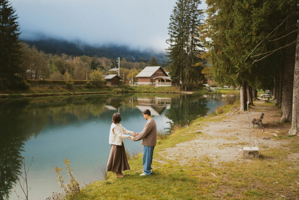 Katya and Michael holding hands by the serene Promenade du Lac des Gaillands in Chamonix, France, during their casual and intimate French Alps elopement. The tranquil lake and majestic mountain backdrop add to the romantic and timeless vibe